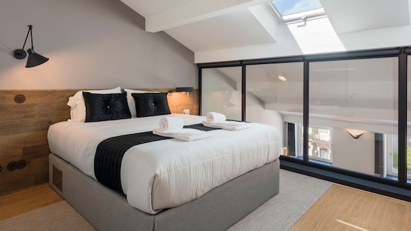 A modern bedroom with a large bed, a skylight, and a balcony with a view.