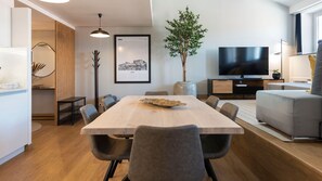 A modern living room with a dining table, chairs, a flat-screen TV, a plant, and a sofa.