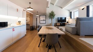 A modern kitchen with a microwave, sink, and cabinets. There is a dining area with a wooden table and chairs, a TV, and a grey sofa.