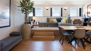 A modern living room with a grey sofa, a wooden dining table, and a large window. - Modern Loft w/ AC in Downtown Porto by LovelyStay (Porto)