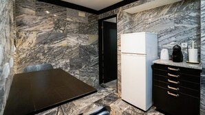 Eine kleine Küche mit Marmor-Spritzschutz, einem weißen Kühlschrank und einer schwarzen Arbeitsplatte mit Kaffeemaschine.