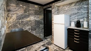 A compact kitchen with a marble backsplash, a white refrigerator, and a black countertop with a coffee maker.