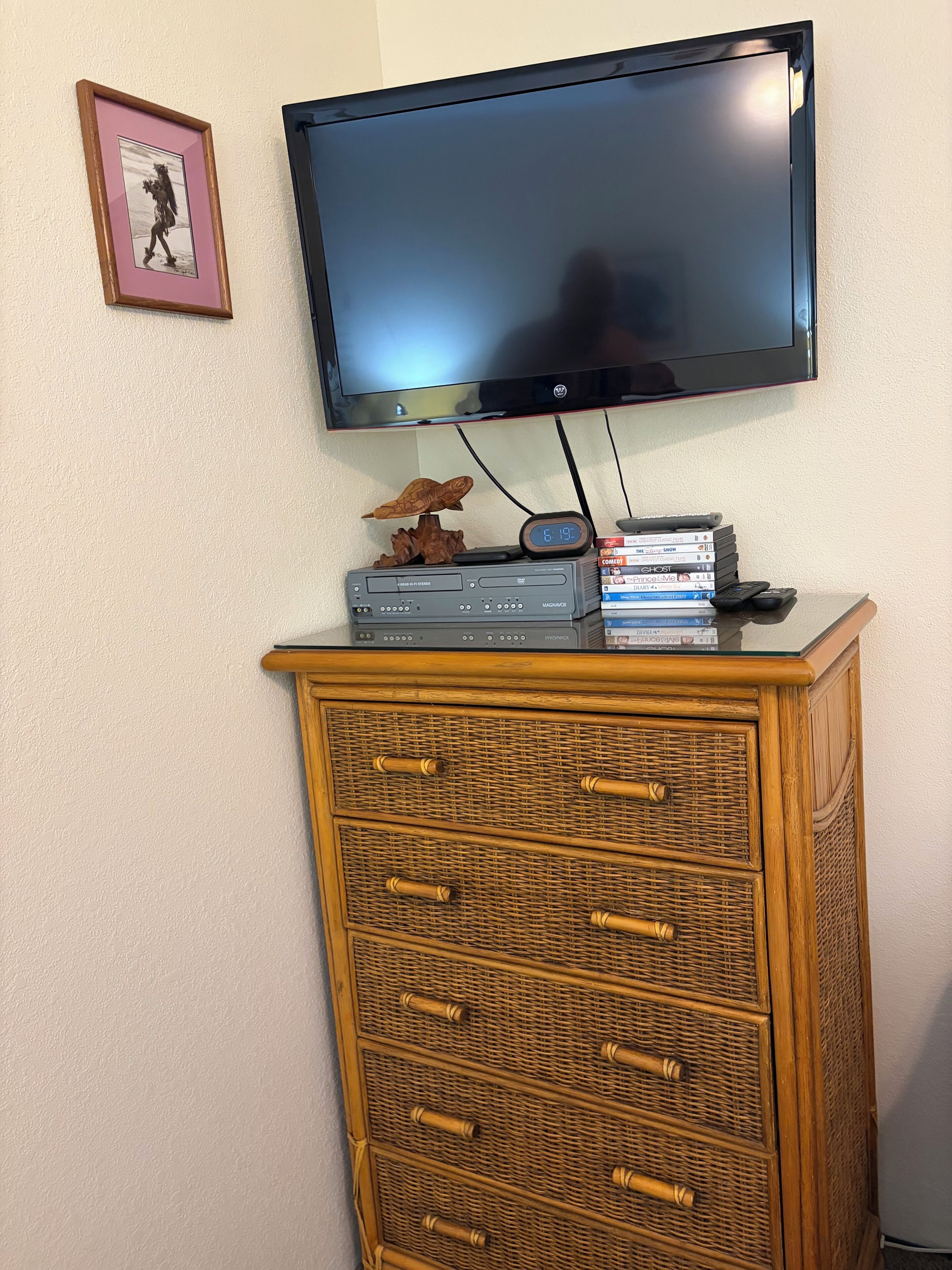 Un téléviseur fixé au mur, un meuble en bois avec des tiroirs et un tableau encadré.