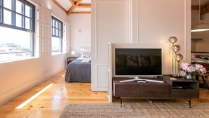 Un dormitorio moderno con una televisión grande, suelo de madera, una cama con ropa de cama floral y vistas amplias a través de ventanas grandes.