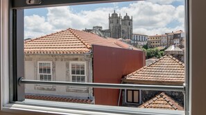 A view through a window of a building with red-tiled roofs, a metal railing, and a historic church in the background.