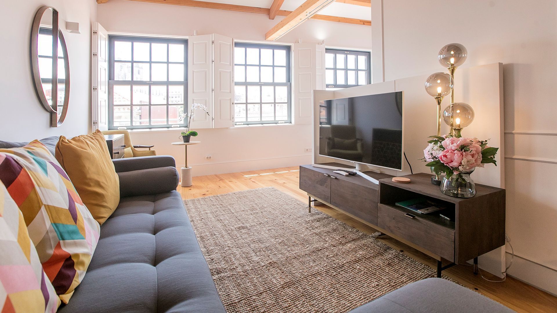 Ett modernt vardagsrum med en grå soffa, en platt-TV och en dekorativ lampa.