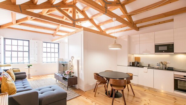 Una cocina moderna con armarios blancos, un comedor con sillas de madera y una sala de estar con un sofá y una mesa de centro.