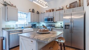 Una cocina moderna con gabinetes blancos, electrodomésticos de acero inoxidable, encimera de mármol y taburetes de madera.