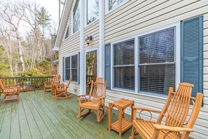 A wooden deck with outdoor furniture, including chairs and a table, and a house with large windows and shutters.