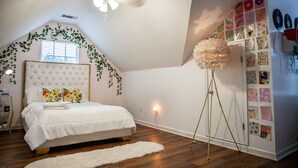 Un dormitorio con una cama, ventilador de techo, alfombra blanca y una pared decorada.
