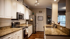 Una cocina con armarios blancos, encimeras de granito, horno de acero inoxidable y refrigerador.