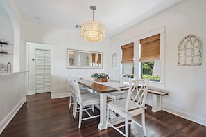 Un coin repas avec une table en bois et des chaises blanches, un luminaire suspendu et un grand miroir au mur.
