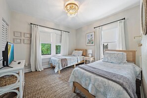 Quarto com duas camas, televisão e janela com cortinas.
