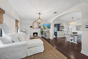 Uma sala de estar espaçosa com um sofá branco, lareira e um espaço de jantar com mesa e cadeiras.