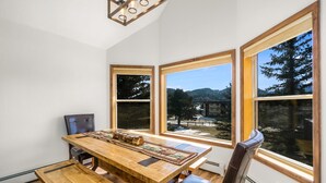 A dining area with a wooden table, chairs, and large windows offering a view of trees and mountains. - Spacious Family Getaway, King Beds, Hot Tub, RMNP (Estes Park)