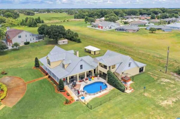 A large house with a swimming pool, surrounded by a well-maintained lawn and a few trees.