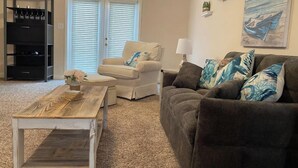 Een woonkamer met een bank, fauteuil, bijzettafeltje en een boekenkast.