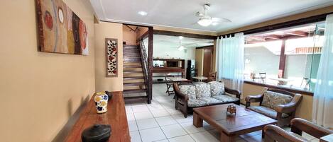 Amplia sala de estar con una mesa de centro de madera, un sofá y una mesa de comedor. Una escalera conduce a un nivel superior.