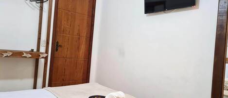Una habitación con cama, un armario de madera, un televisor montado en la pared y una toalla sobre la cama.