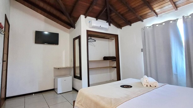 A bedroom with a bed, a TV, a wardrobe, and an air conditioning unit. - Centro UP (Búzios)
