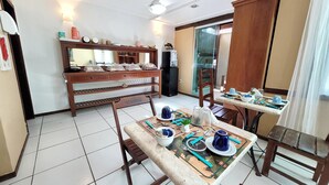 A dining area with a table set for two, a wooden cabinet, and a ceiling fan. - Centro UP (Búzios)