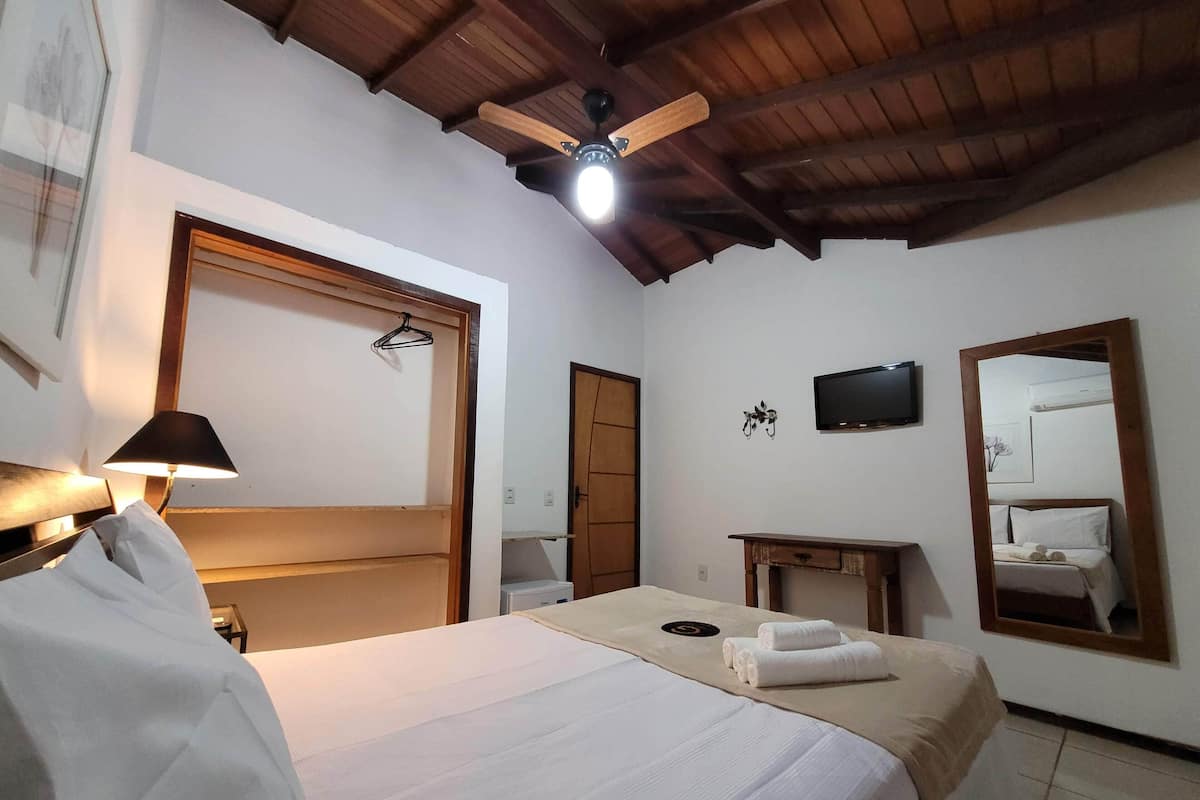 A hotel room with a bed, a desk, a mirror, a ceiling fan, and a TV.
