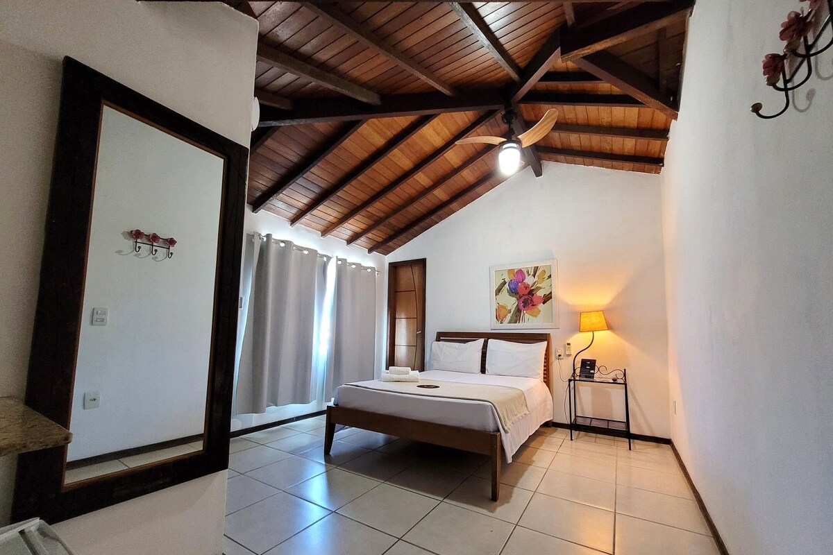 A bedroom with a bed, a ceiling fan, a nightstand, and a wall-mounted lamp.