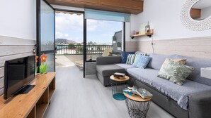 A modern living room with a grey sofa, a flat-screen TV, a wooden coffee table, and a balcony with a view of the mountains. - Home2Book Cozy Helmut's Place Corralejo, Terrace (Corralejo)