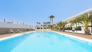 A swimming pool with lounge chairs, palm trees, and a building with balconies. - Home2Book Cozy Helmut's Place Corralejo, Terrace (Corralejo)
