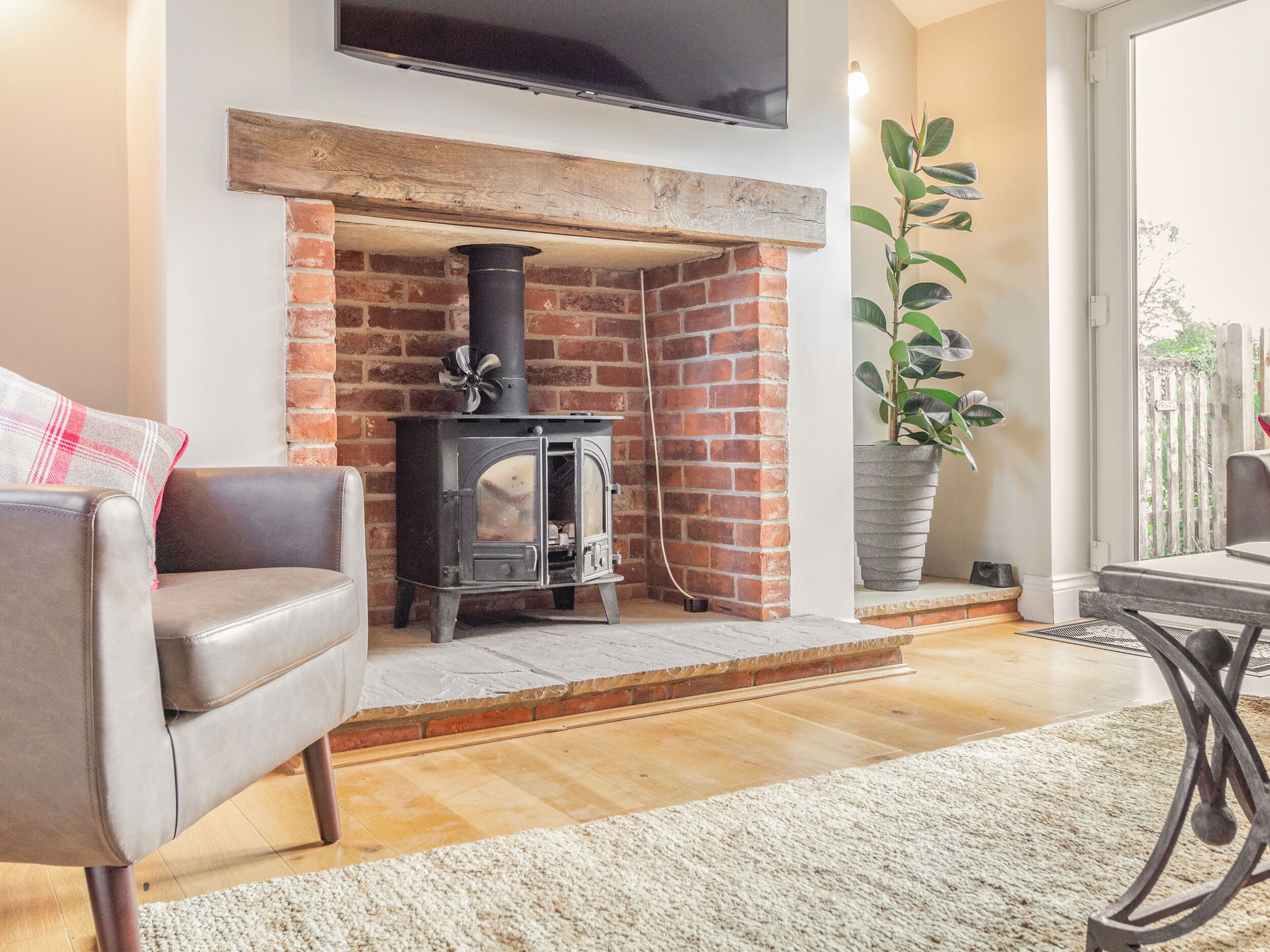Ein Wohnzimmer mit Kamin aus Ziegelsteinen, einem Ledersofa, einer Topfpflanze und einem Fernseher, der über dem Kamin angebracht ist.