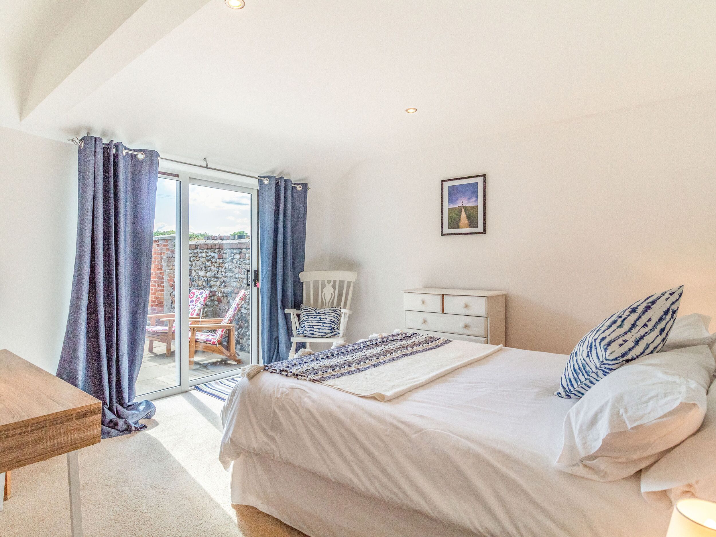 A bedroom with a large bed, a chair, a dresser, and a view of a garden through a glass door.