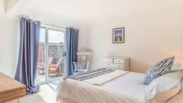 A bedroom with a large bed, a chair, a dresser, and a view of a garden through a glass door.