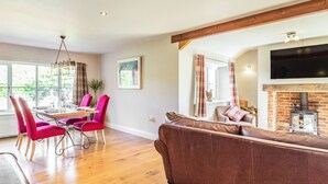 A modern living room with a wooden floor, a brown sofa, a dining area with pink chairs, and a fireplace with a TV above it. - The Croft (Thetford)