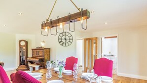 A dining room with a wooden table set for four, surrounded by red chairs. A grandfather clock and a wall clock are visible. - The Croft (Thetford)