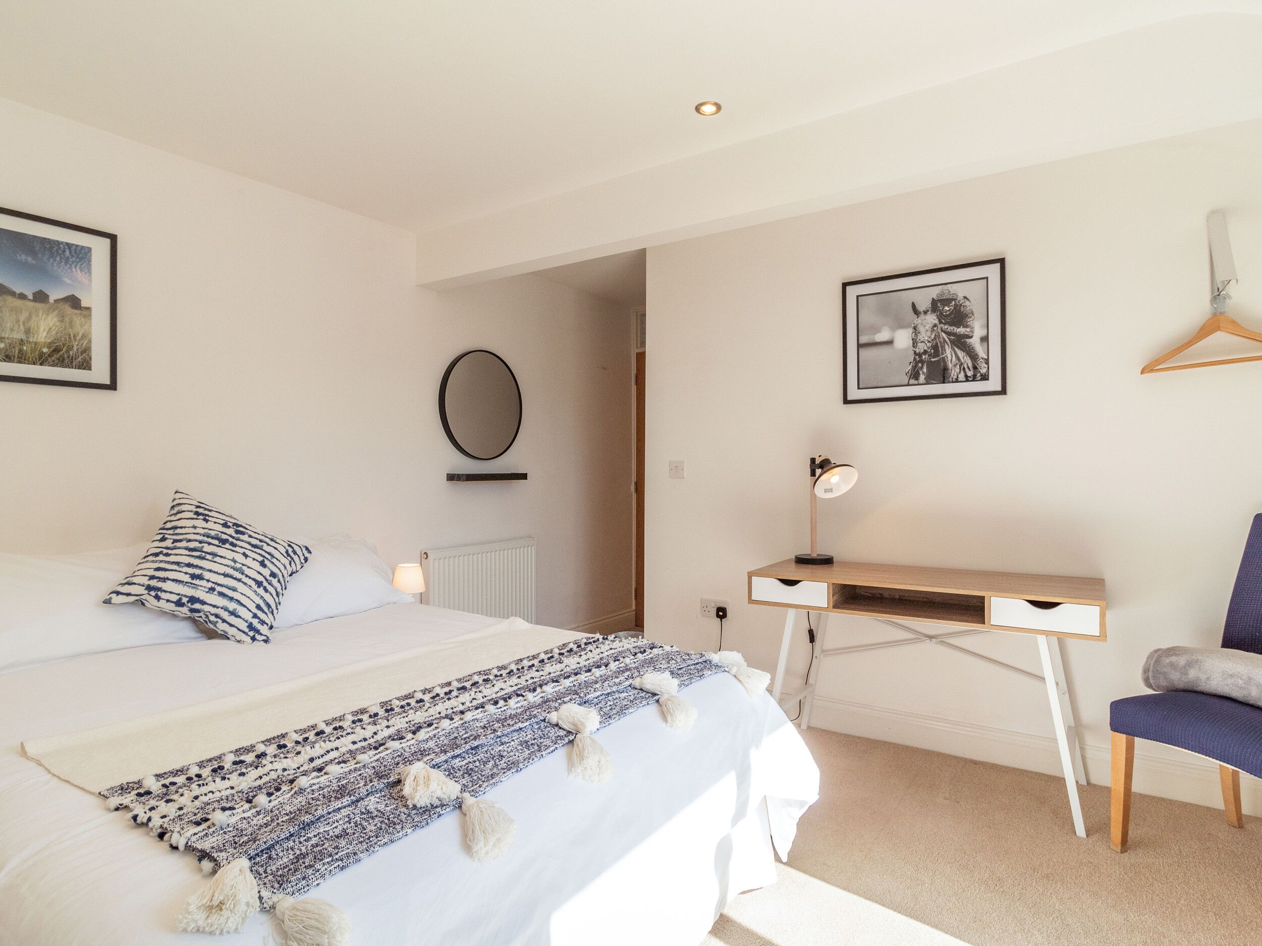 A bedroom with a bed, a desk, a chair, a radiator, a mirror, and two framed pictures on the wall.