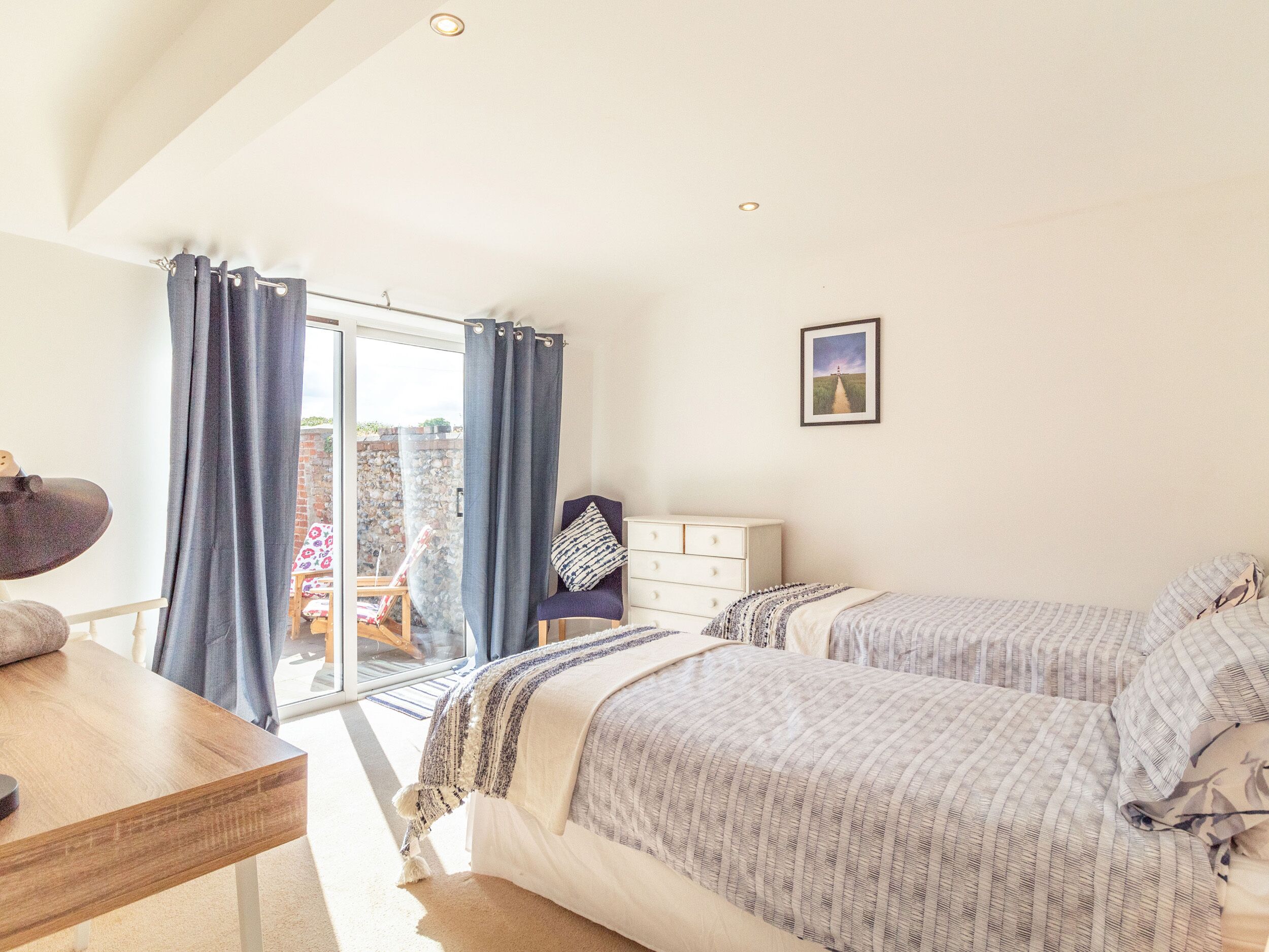 A bedroom with two beds, a desk, a chair, and a view of the outdoors through a glass door.