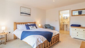 A bedroom with a wooden bed, bedside lamps, a chair, a dresser, and a bathroom visible through an open door. - The Croft (Thetford)