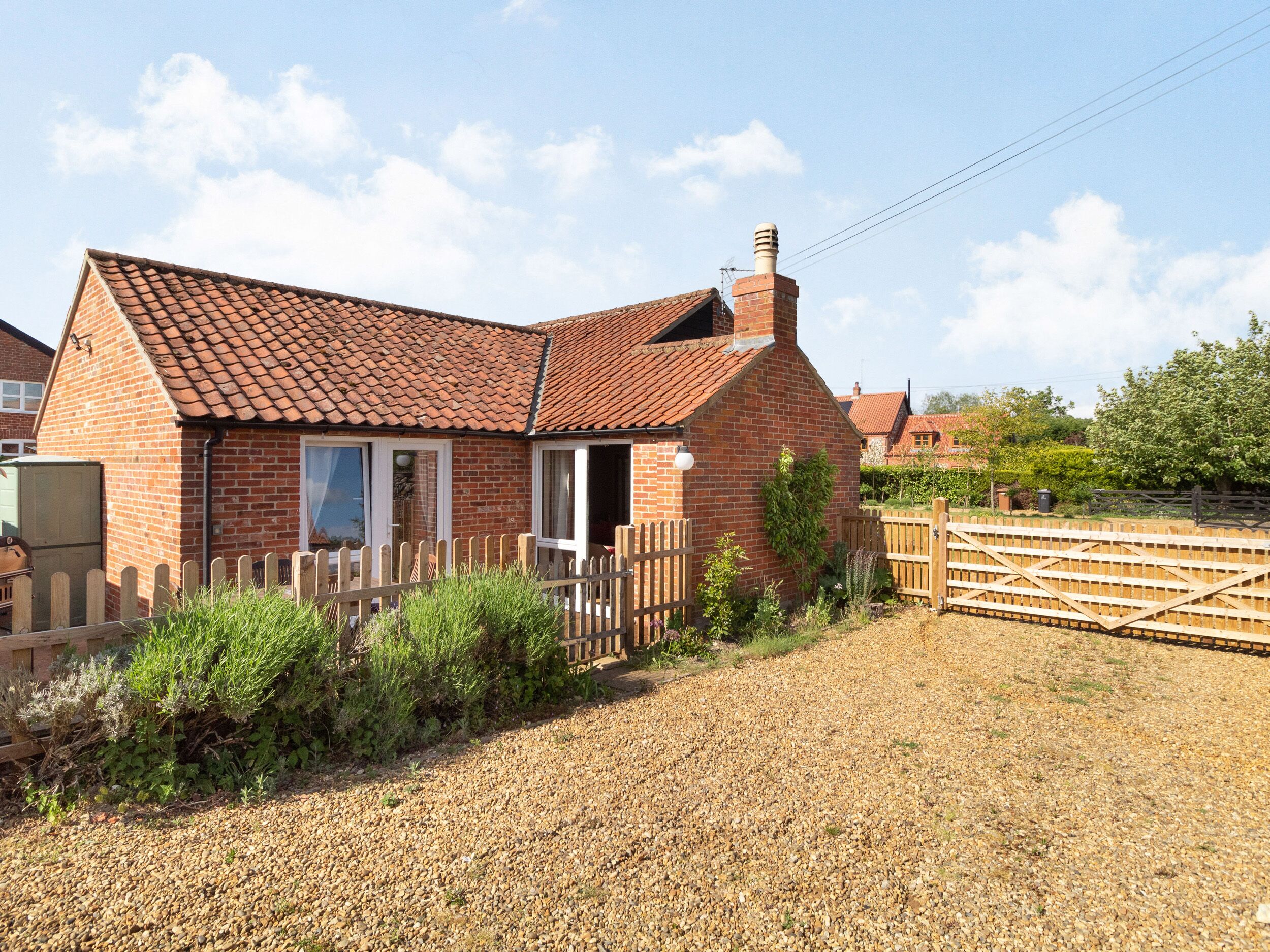A brick house with a tiled roof, a wooden fence, and gravel driveway.