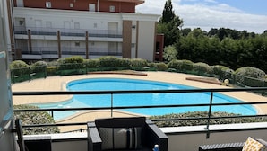 Un balcon avec des meubles d’extérieur, une piscine et un bâtiment en arrière-plan.