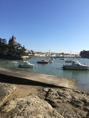 A harbor with boats docked, a castle-like building, and a rocky shoreline.