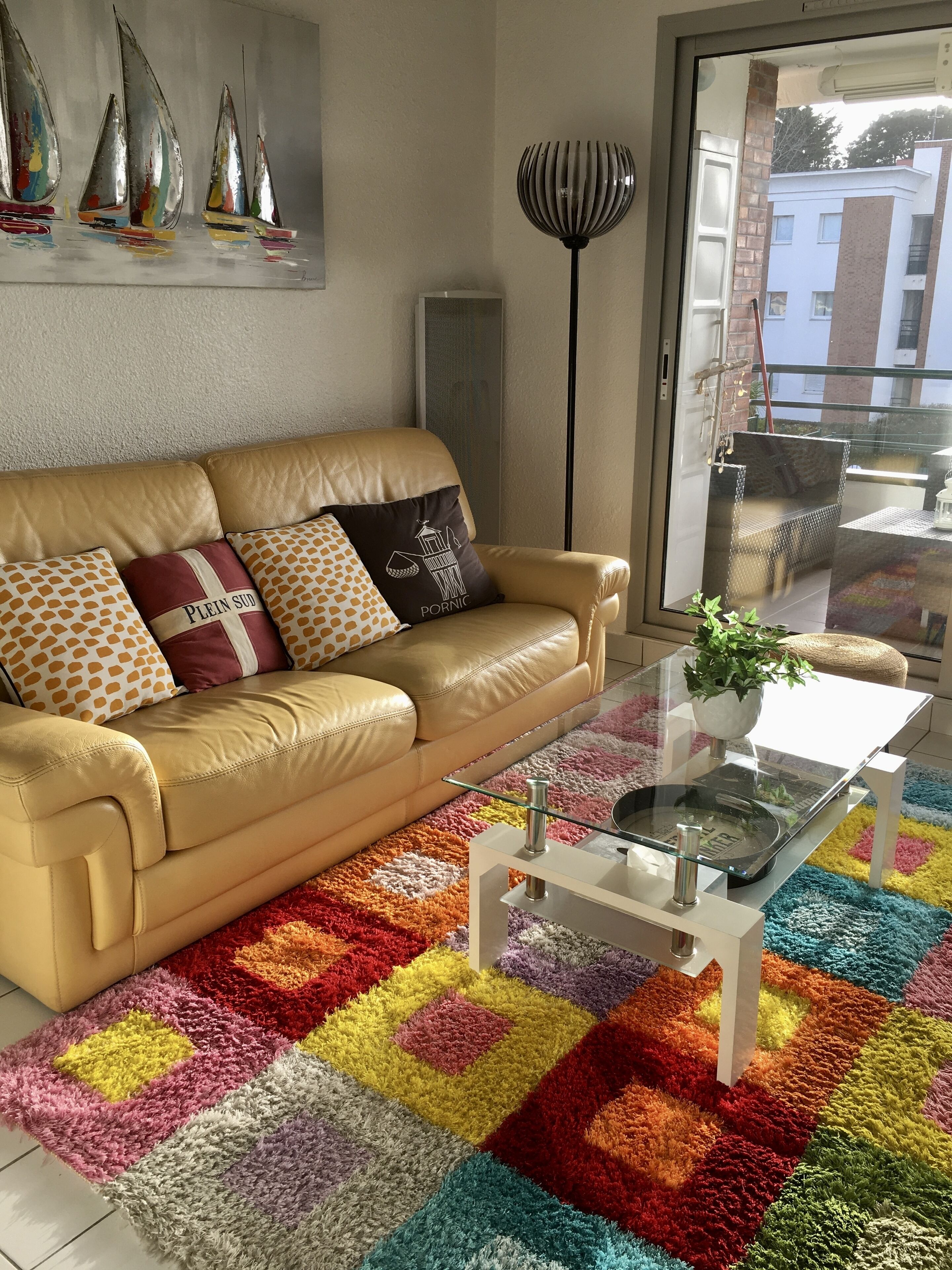 A living room with a beige sofa, colorful rug, and a glass coffee table.