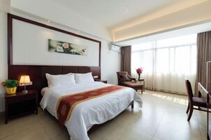 Una habitación de hotel con una cama grande, un escritorio, una silla, una mesita de noche con lámpara y un cuadro en la pared.