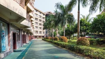 A hotel corridor with a green pathway, palm trees, and a building with multiple floors and balconies.