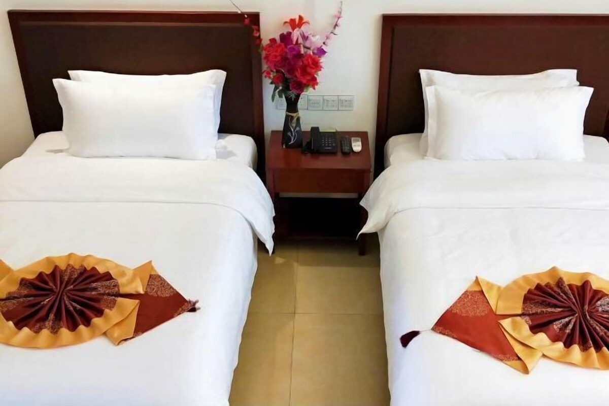 A hotel room with two beds, white bedding, a nightstand with a vase of flowers, and a telephone.