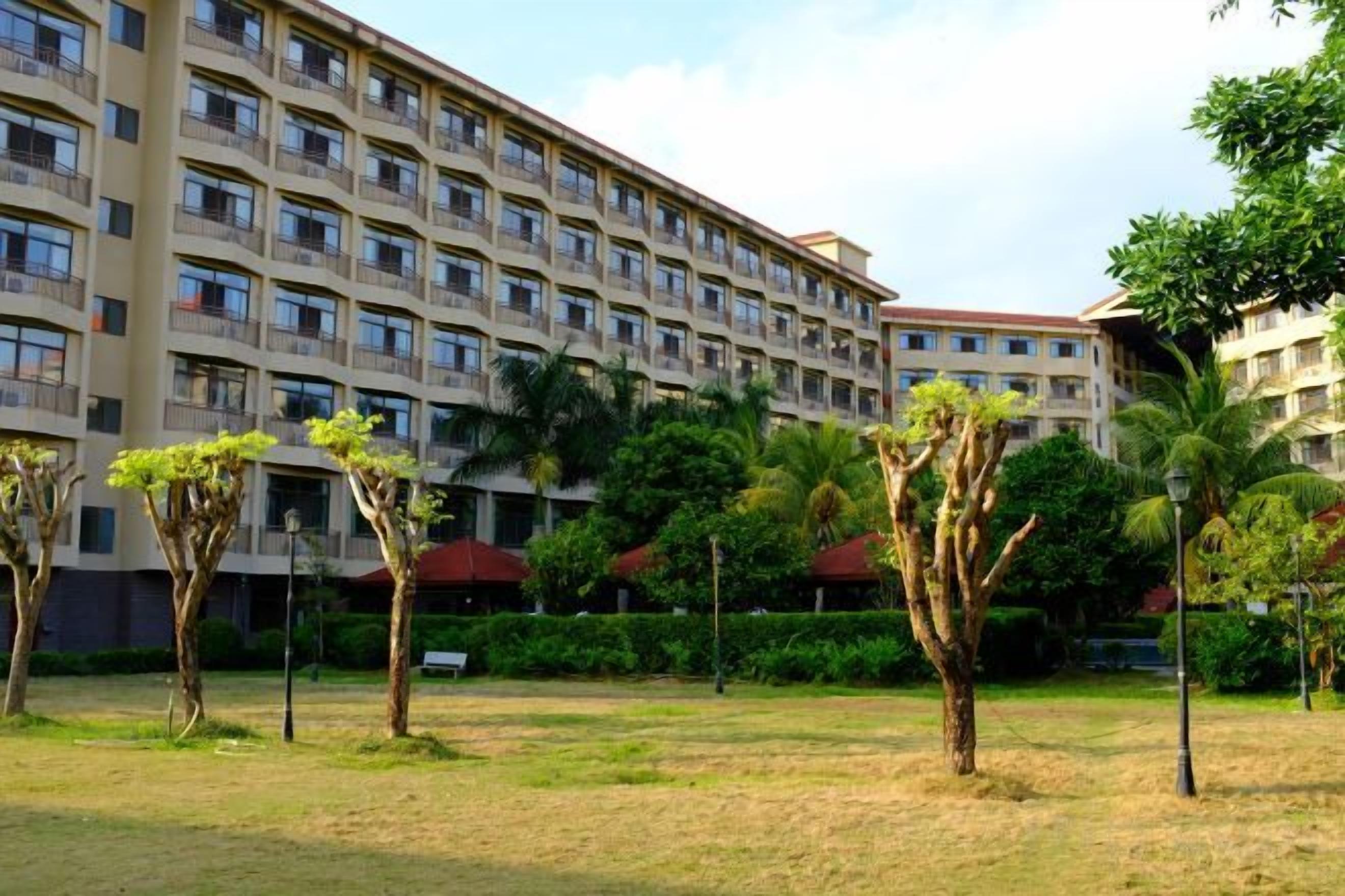 A multi-story hotel with a courtyard featuring palm trees and a well-maintained lawn.