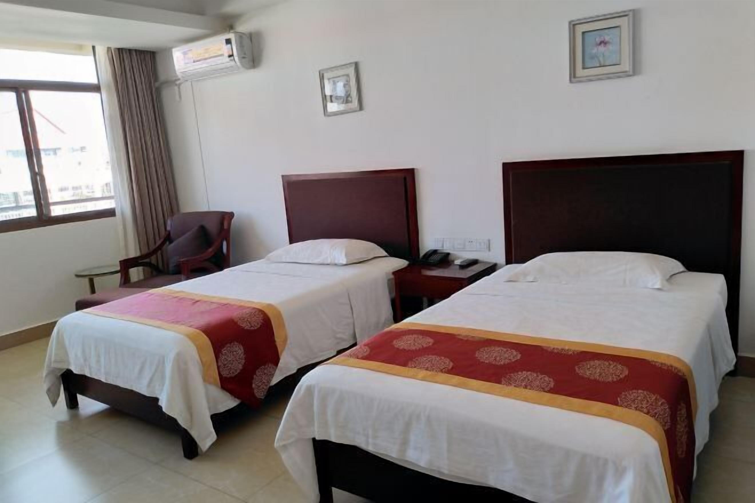 A hotel room with two beds, a chair, a desk, and a window with curtains.
