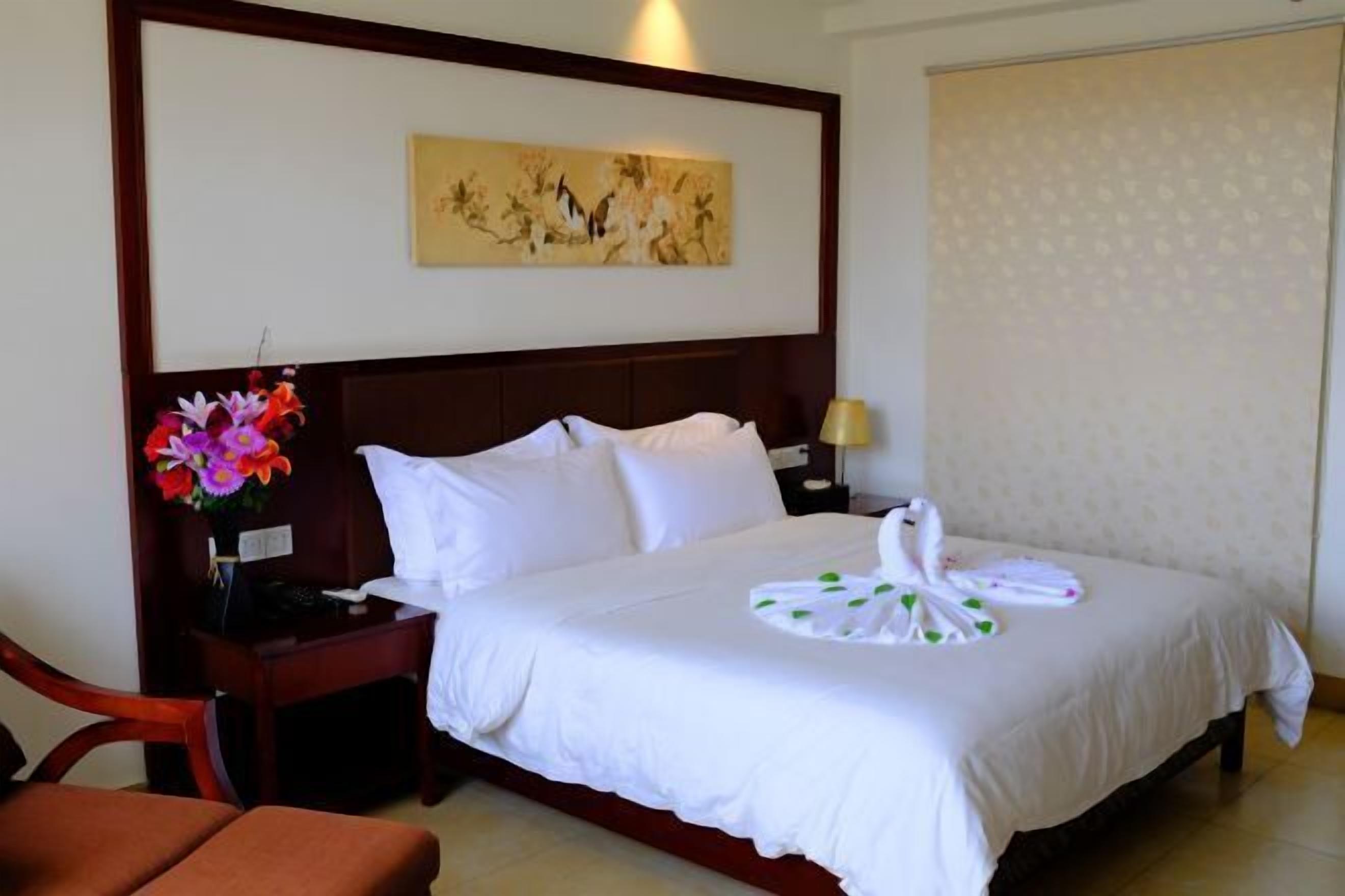 Una habitación de hotel con una cama, una mesita de noche, una lámpara, una silla y un cuadro en la pared.
