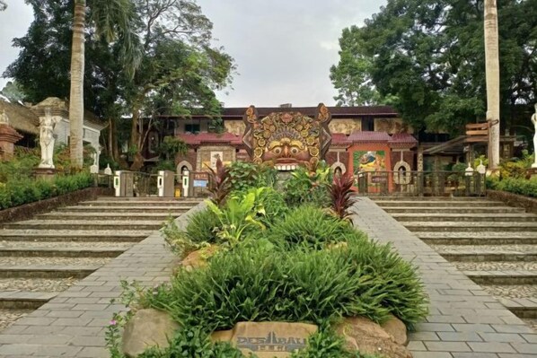 A traditional building with a central entrance, steps leading up to it, and a garden area in the foreground.
