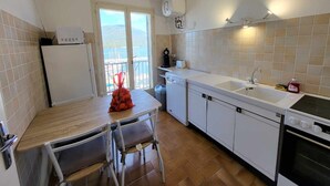 A compact kitchen with a wooden table, two chairs, a built-in oven, a dishwasher, and a large window offering a view of the sea. - Apartment rental Propriano (Propriano)