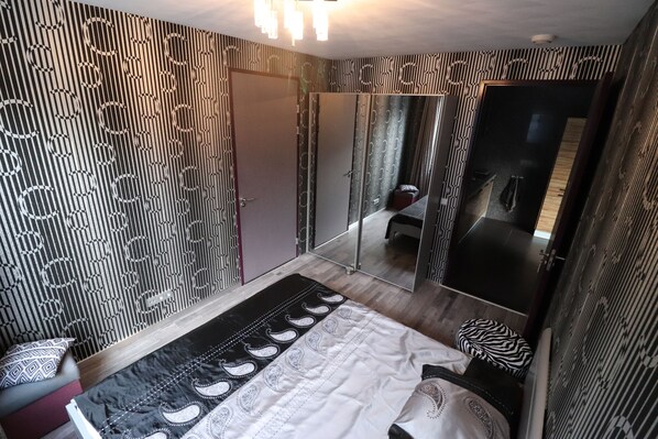 A bedroom with a bed, a mirror, and patterned wallpaper. - New accommodation. (Venray)